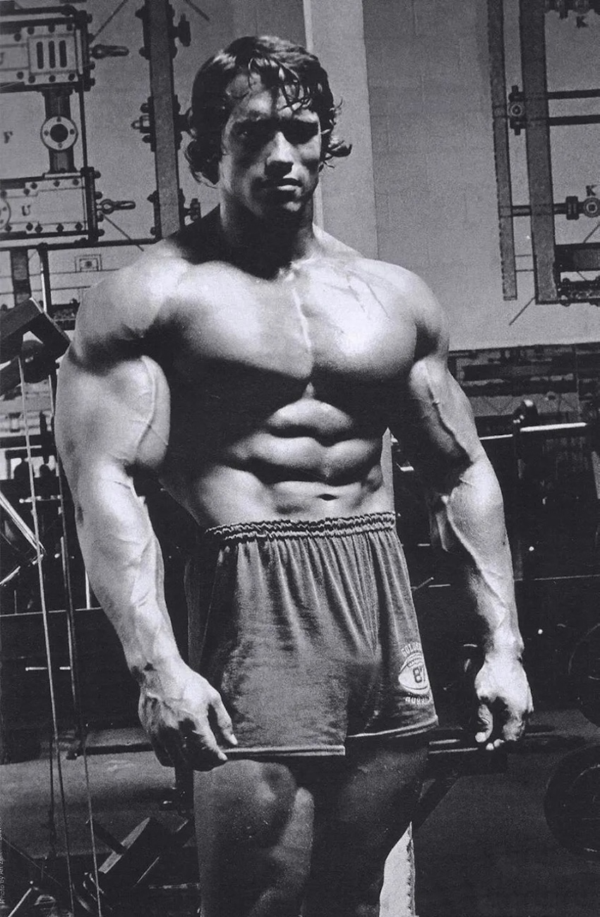 Arnold Swarchenegger edzés utánni erős teste ahogy pózol a tükörben.