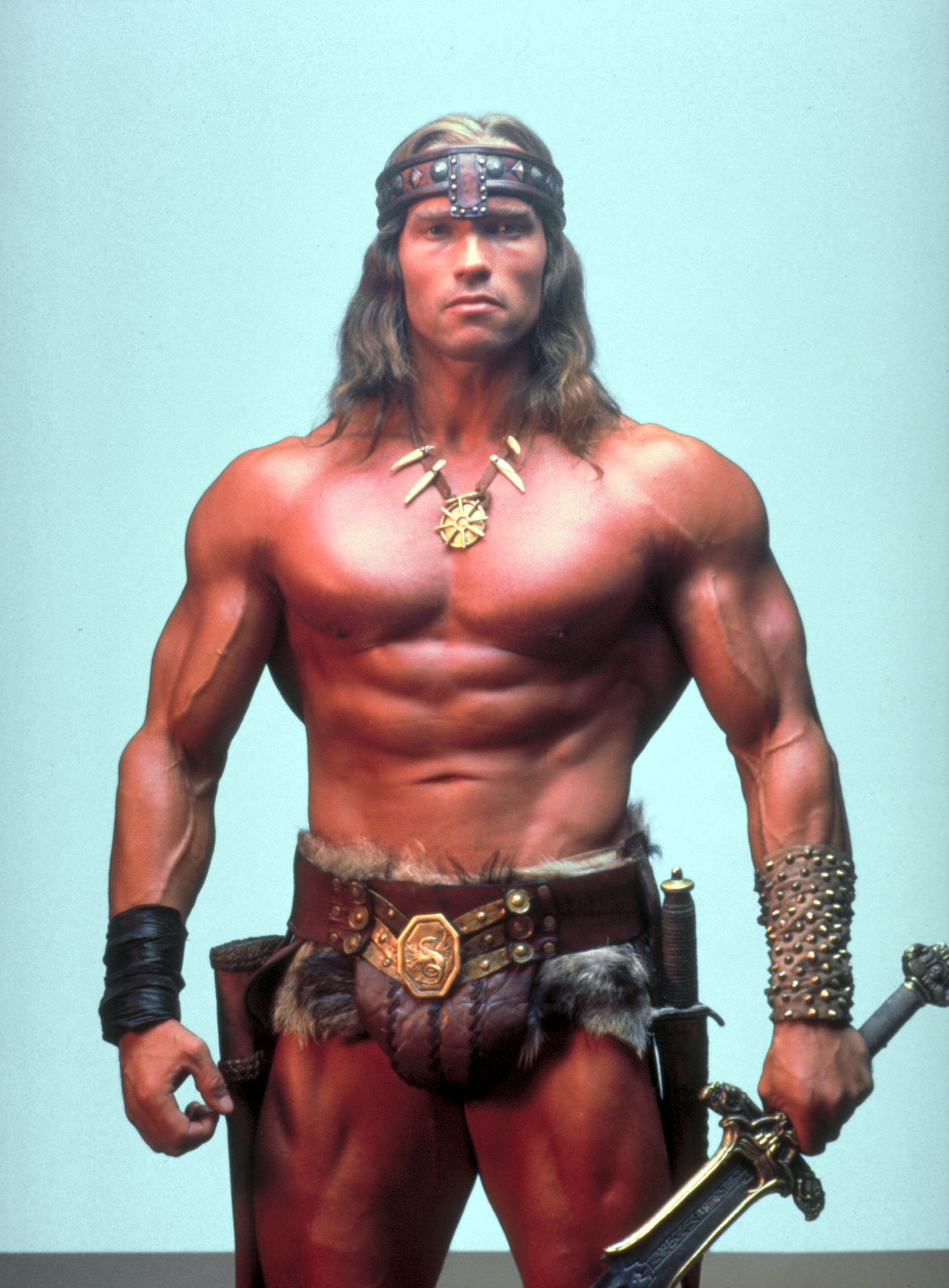 Arnold Swarchenegger amikor a Conan a barbár filmben szerepelt, erős izmokkal és ősember ruhában.