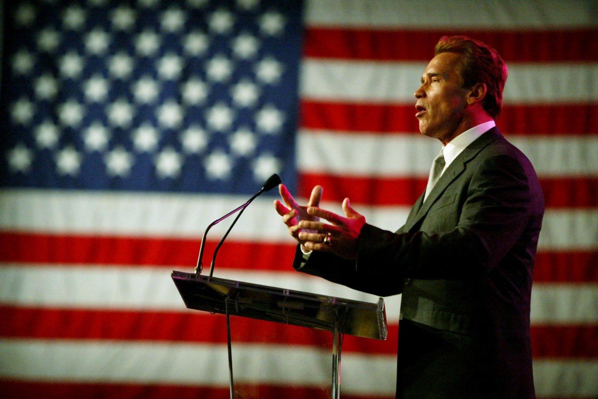 Arnold Swarchenegger beszédet mond mögötte a USA zászlója