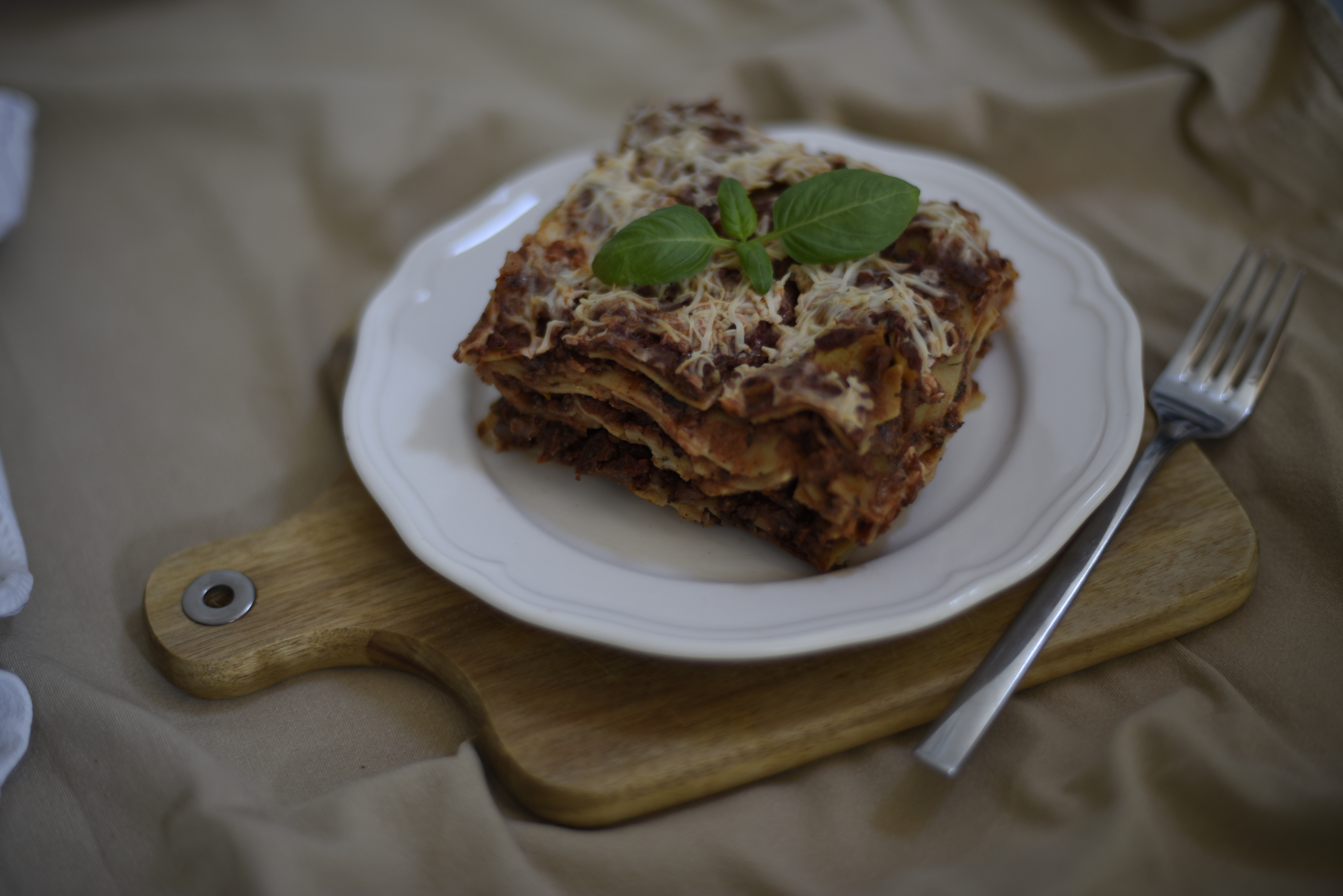 Lasagne egy tányéron, bazsalikommal és vegán sajttal a tetején