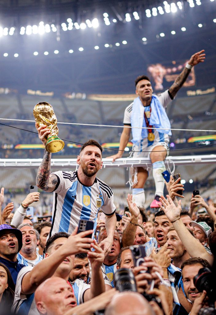 Messi ünnepel nagy tömegben kezében a világbajnoki kupával valakinek a nyakában