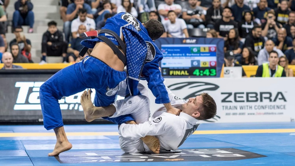 The fighter in white Gi tries to submit his opponent with an ankle lock.