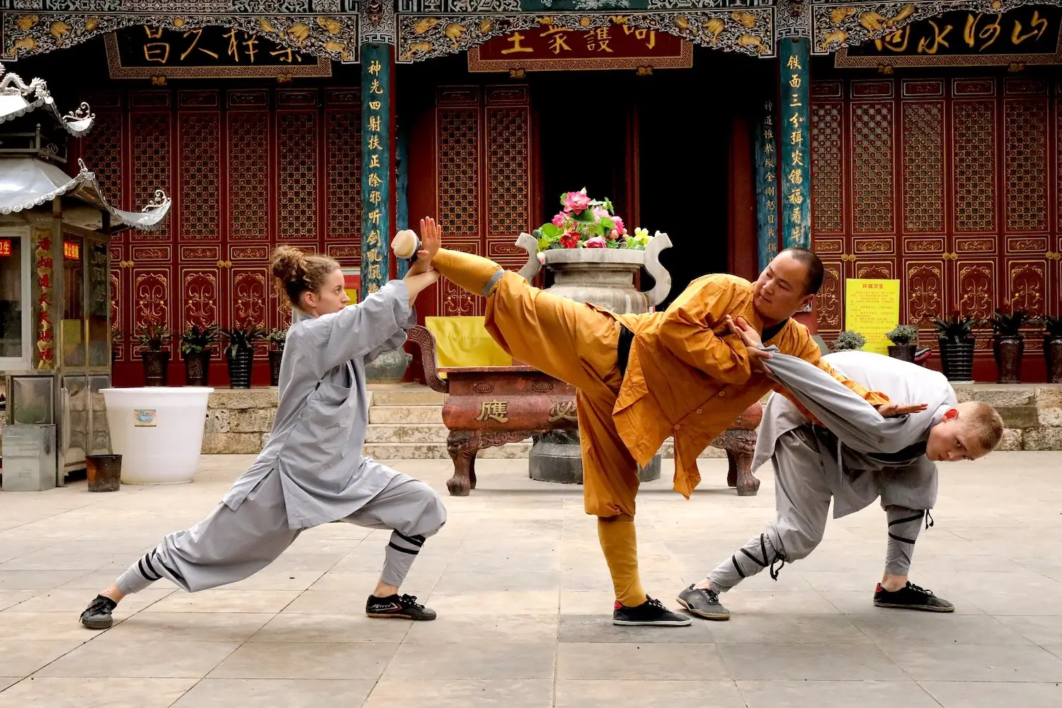 A Shaolin Monk in orange demonstrates Kung Fu against two attackers.