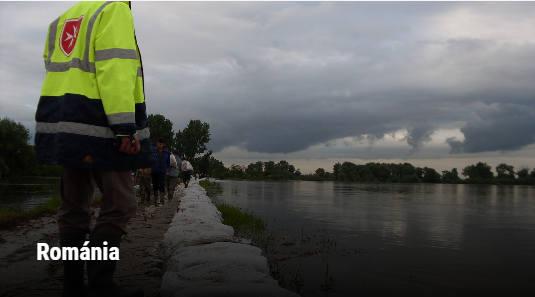 Homokzsákokkal megerősített gát mellett vonuló segélycsapat a Tisza árvízvédelmi tölcsérénél Romániában