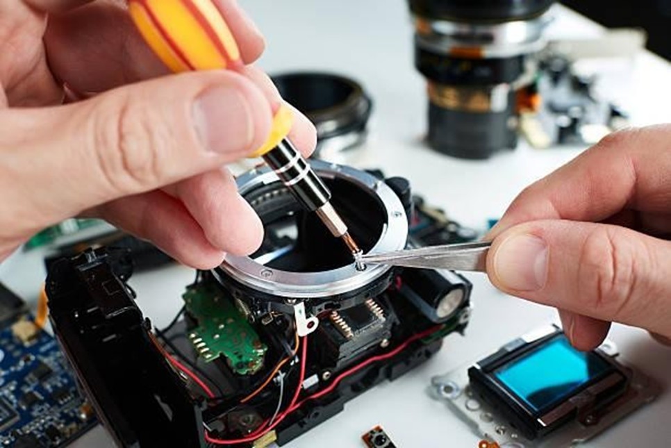 Close-up shot of a person repairing a disassembled digital camera, with different parts laid alongsides the table.