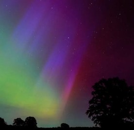 A colorful shot of Aurora Borealis with intense green and red colours, and faint stars in the background.
