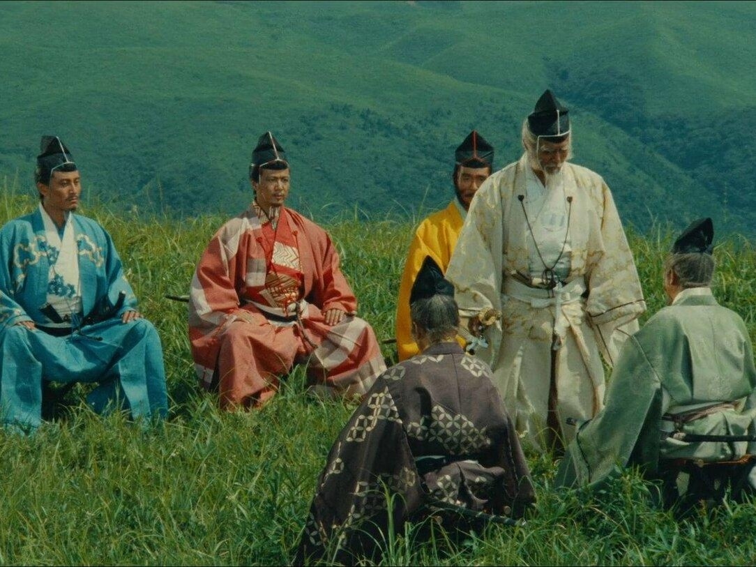 Scene from 'Ran', where samurai are sitting in grass and another one is talking to them