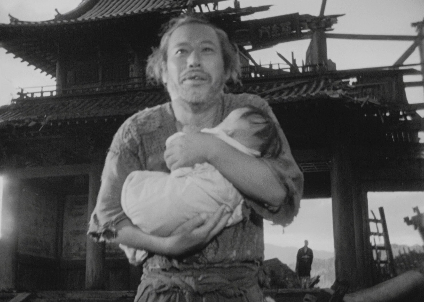 Scene from 'Rashomon', where an elderly man is holding a baby in front of a crumbling building