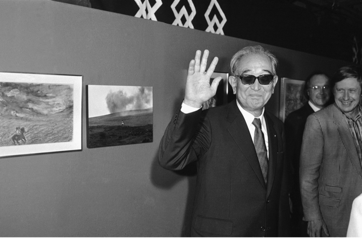 Older Akira Kurosawa waving at the camera in a gallery